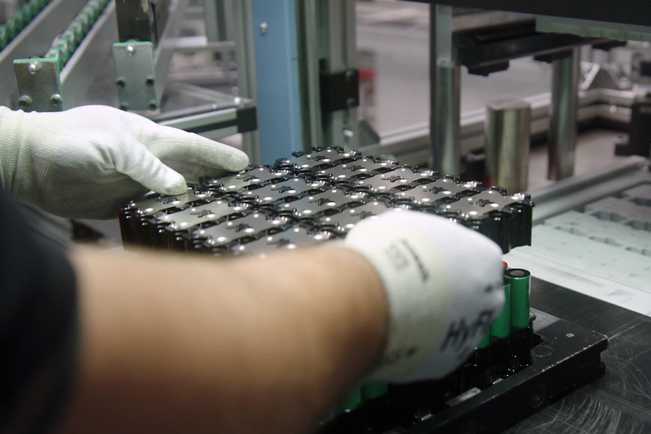 A man wearing work gloves places the top cell holder with cell connector plates onto the bottom one to join the battery cells together