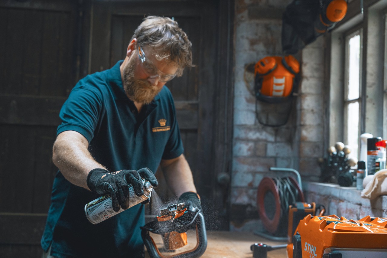 A man in a workshop sprays a hedge trimmer with STIHL Superclean