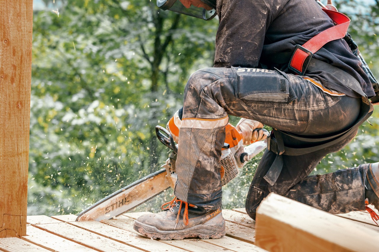 A person wearing work boots and STIHL Advance X-Light trousers sawing a wooden platforom edge with a STIHL chainsaw