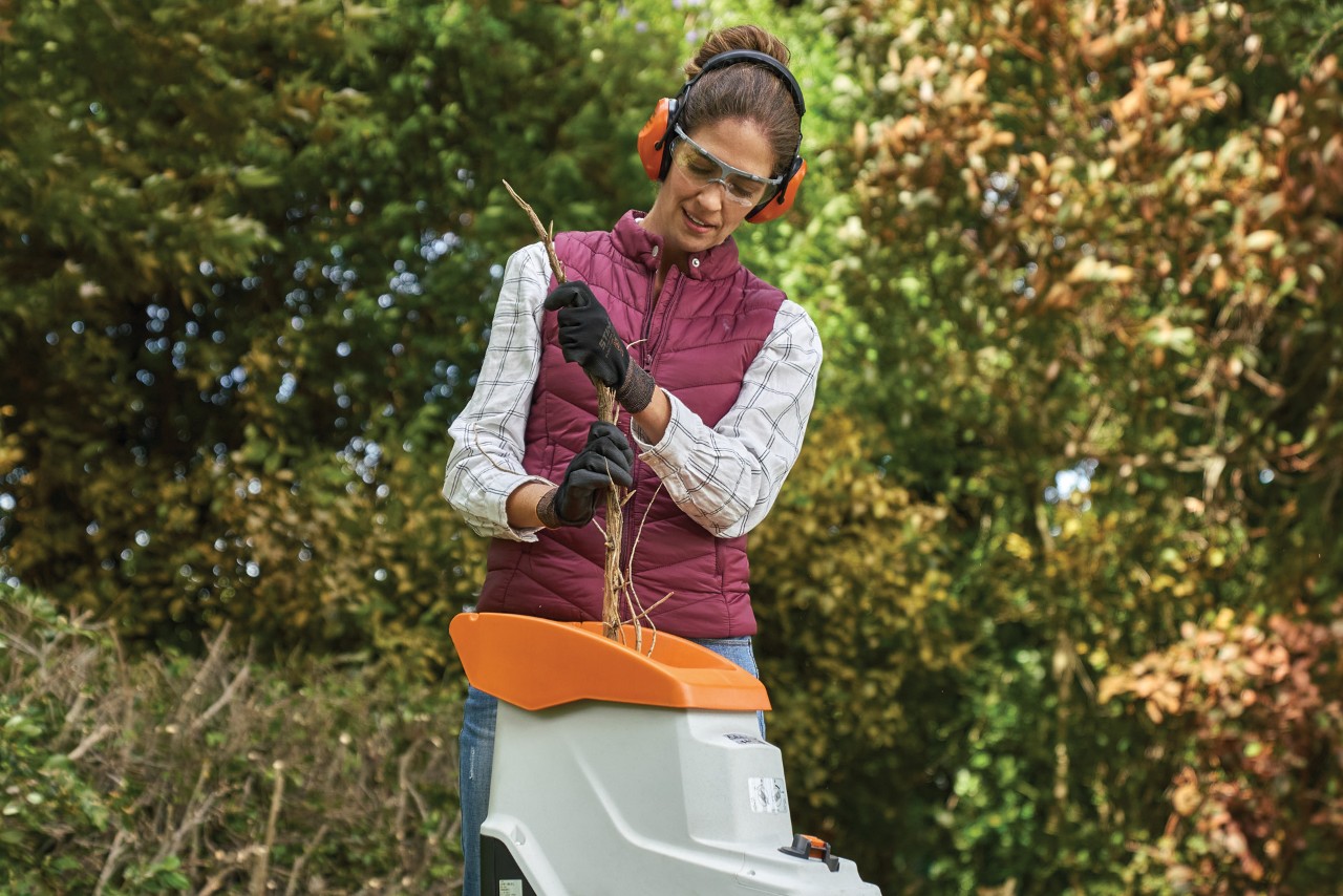 A woman wearing ear protection headphones and gloves works with some garden equipment at home