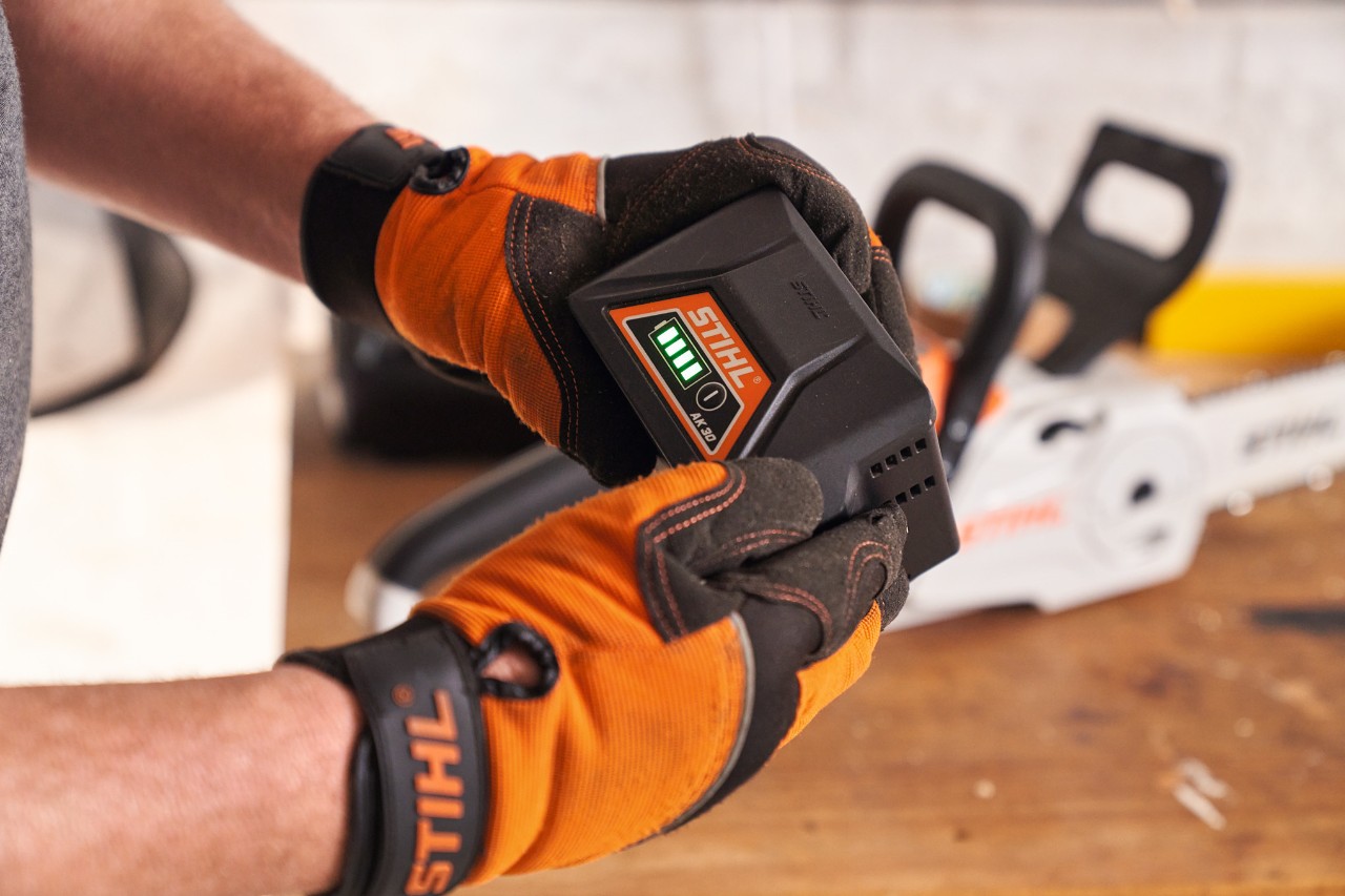 A person wearing STIHL protective gloves holding a STIHL lithium-ion battery in their hands