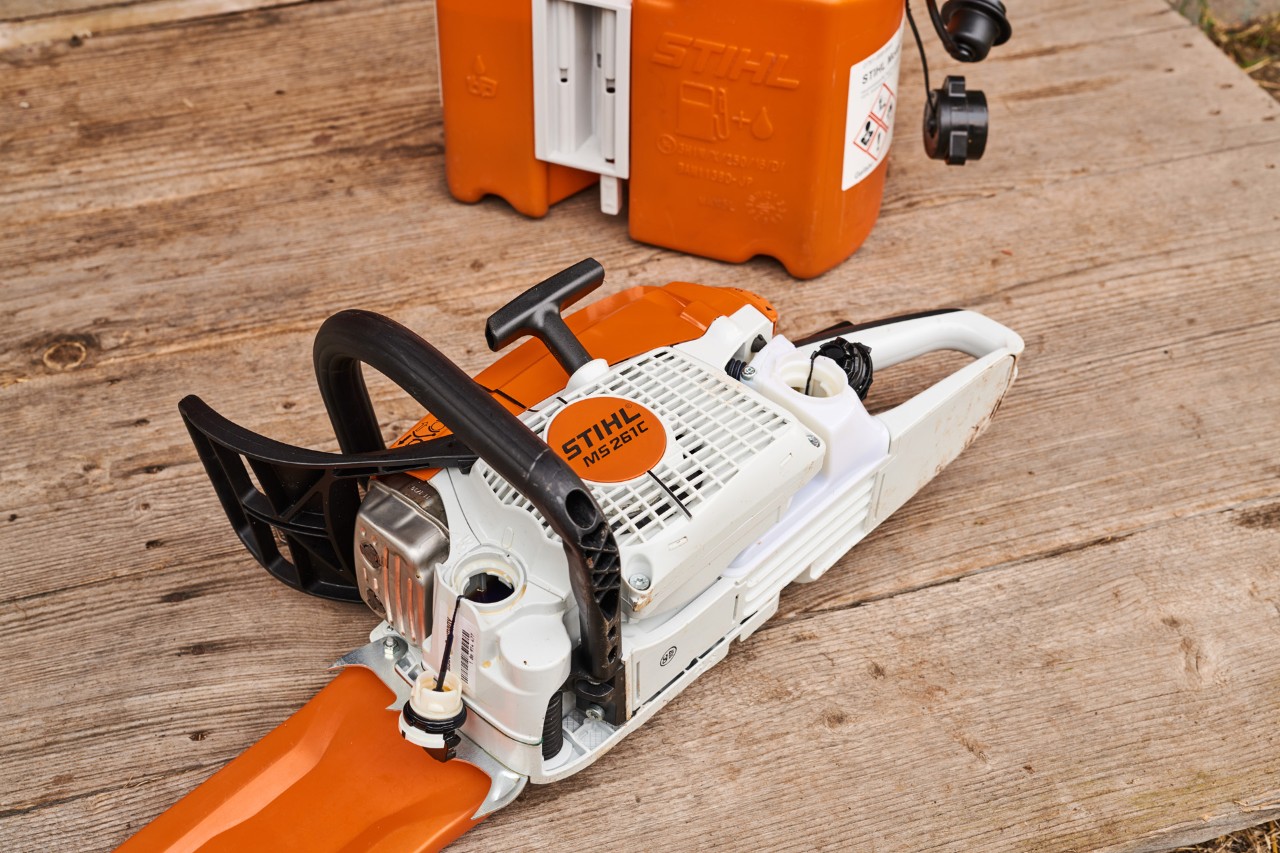 A STIHL MS 261 petrol chainsaw on the floor with the caps for fuel and oil tanks removed.
