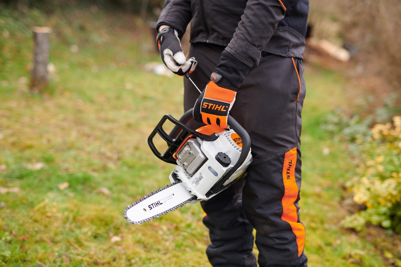 A STIHL 180 C-BE petrol chainsaw with ErgoStart being held by a person in  protective gear
