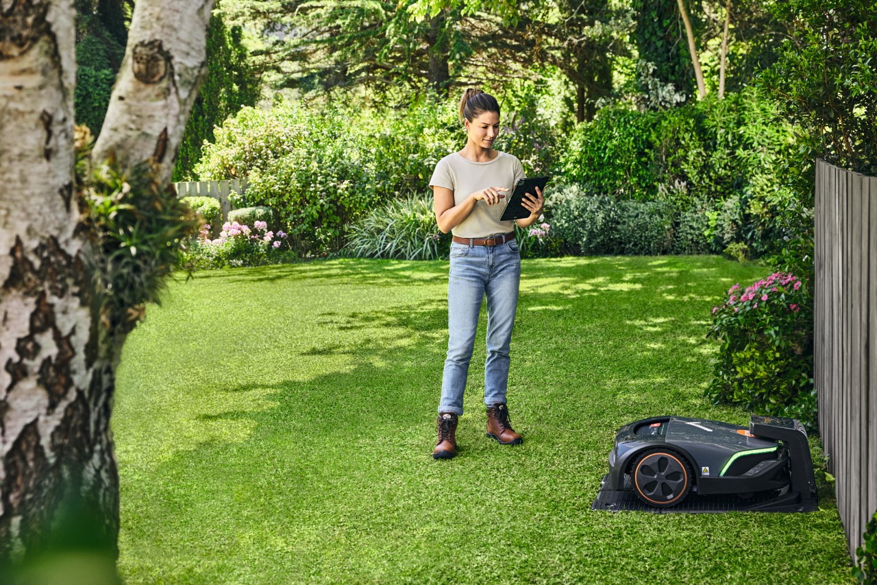 A woman using a tablet in a garden and operating a STIHL iMOW® 522 robot mower