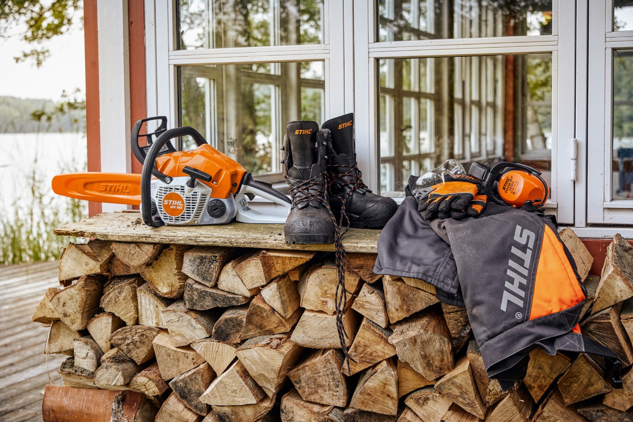 STIHL protective clothing and the MS 162 lying on a shelf above stacked firewood