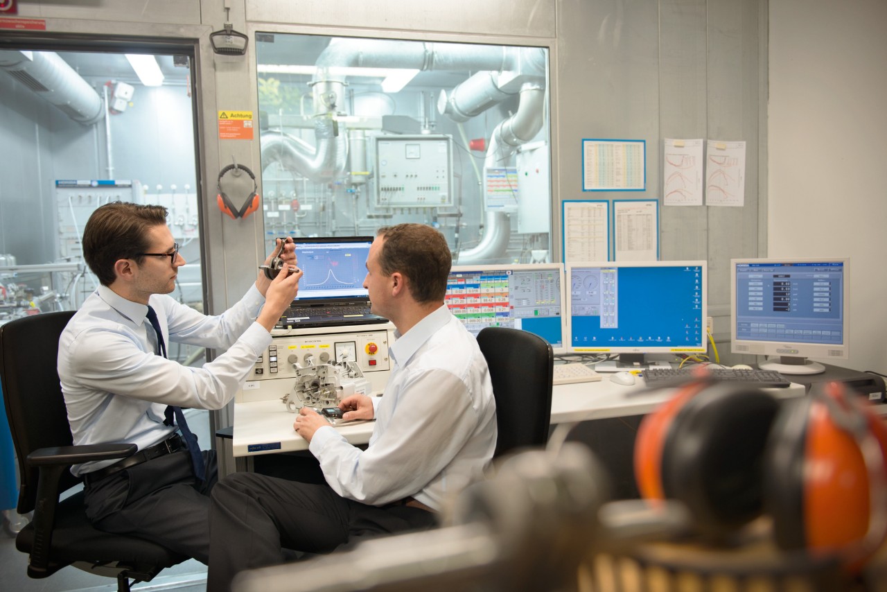 A lab where two men are sitting at a desk with several monitors, assessing components of a new product